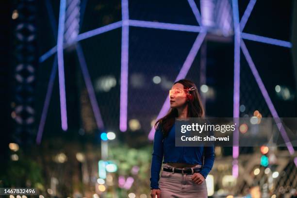 young asian woman using smart glasses standing in front of glowing modern building at night - augmented reality marketing stock pictures, royalty-free photos & images