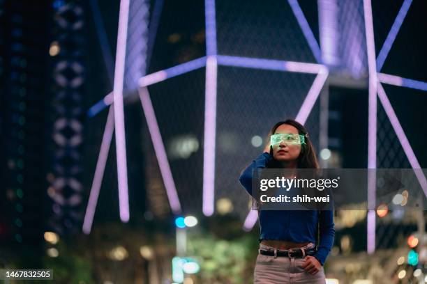 young asian woman using smart glasses standing in front of glowing modern building at night - electronic organiser stock pictures, royalty-free photos & images