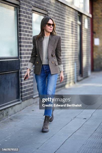 Guest wears brown sunglasses, a pale gray wool pullover, a pale brown wool blazer jacket, blue denim ripped pants, brown suede platform soles ankle...