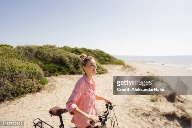 young woman exploring coastline on a bicycle - fietsen genieten stockfoto's en -beelden