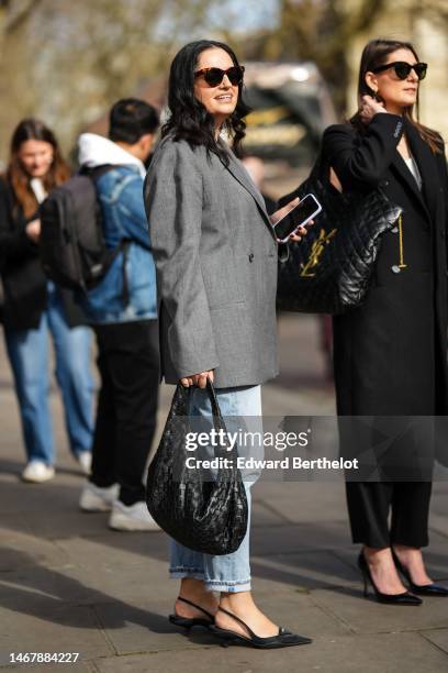 Guest wears brown and black print pattern sunglasses, a white tank-top from Loewe, a gray oversize blazer jacket, blue faded denim pants, a black...