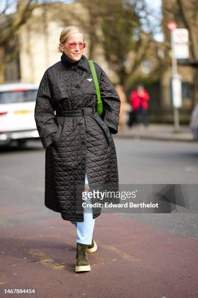 Guest wears pink sunglasses, a black quilted pattern long puffer jacket from Prada, blue faded denim ripped pants, khaki suede ankle boots a green...