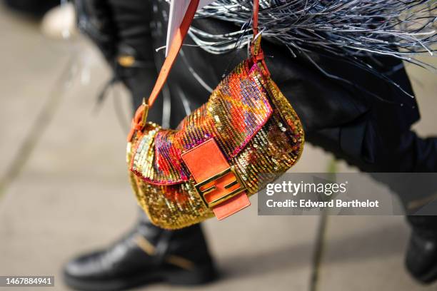 Guest wears a black with white and red print pattern long fringed coat, a black midi skirt, black shiny leather knees boots, a gold and orange...