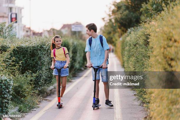 brother and sister riding with scooter in the city with backpack. two kids biking on way to school. copy space. - girl riding scooter stock pictures, royalty-free photos & images