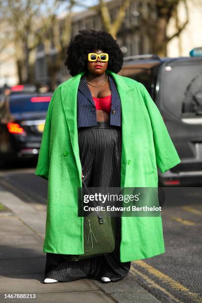 Guest wears yellow square sunglasses, a gold necklace, a red bra underwear, a navy blue striped print pattern cropped blazer jacket, a neon green...