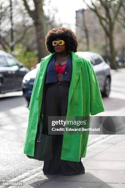 Guest wears yellow square sunglasses, a gold necklace, a red bra underwear, a navy blue striped print pattern cropped blazer jacket, a neon green...