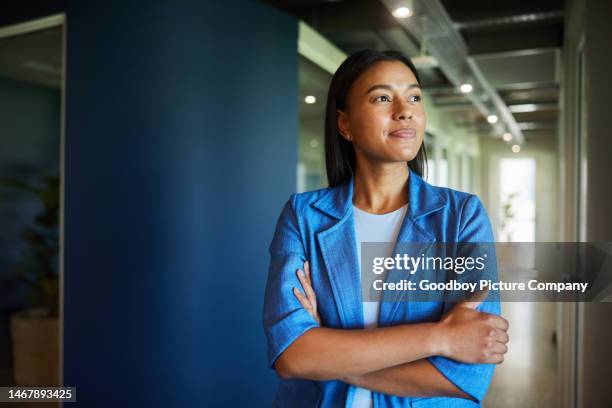 young businesswoman standing with her arms crossed in an office hallway - looking away stock pictures, royalty-free photos & images