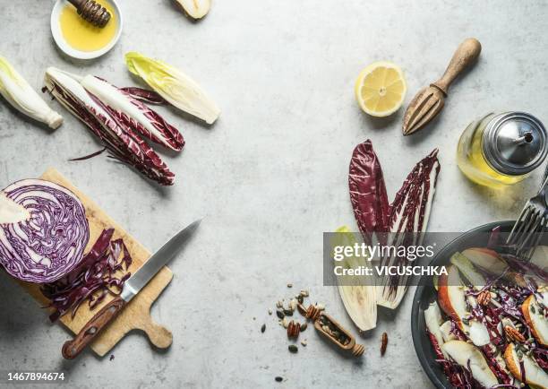 food background with salad ingredients: halved chicories, red cabbage, lemon, honey and olive oil , nuts and seeds - radicchio stock-fotos und bilder