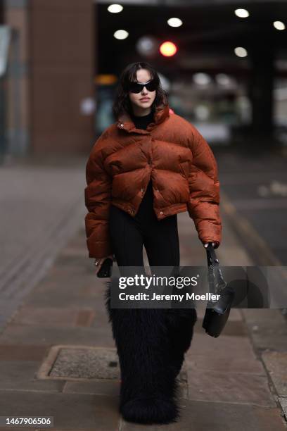 Nastya Burlaka wears Balenciaga black sunglasses, black wool turtleneck pullover, camel / brown / rust red short puffer jacket, black legging pants,...