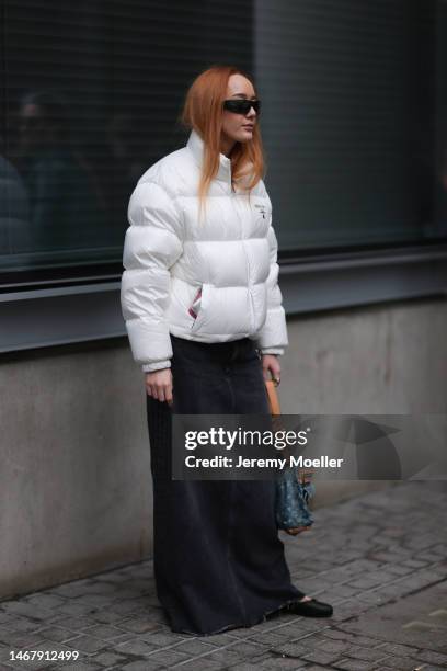 Guest wears Prada Sport black sunglasses, Prada white nylon puffer jacket, black / dark grey denim / jeans long skirt, black leather mules /...