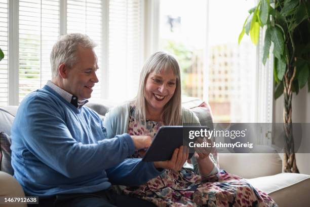 caucasian couple in 50s and 60s using digital tablet - couple on sofa stock pictures, royalty-free photos & images