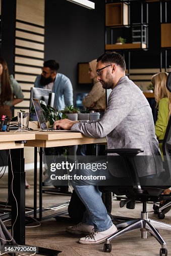 A young man gets in the zone as he works on his laptop at his desk in the office, tuning out distractions and focusing on his tasks at hand A young man gets in the zone as he works on his laptop at his desk in the office, tuning out distractions and focusing on his tasks at hand