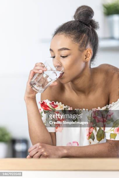 a smiling pretty young woman drinks clean water from a glass leaning on the kitchen table. - törstig bildbanksfoton och bilder