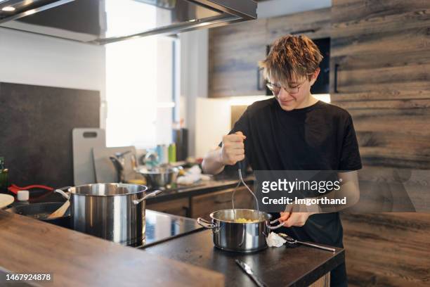 teenage boy helping with meal preparation in kitchen - potato masher stockfoto's en -beelden