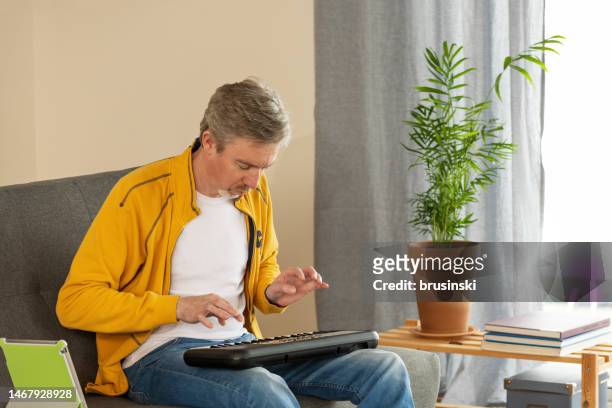 white 50 year old male learning to play synthesizer, using digital tablet - electric piano stock pictures, royalty-free photos & images