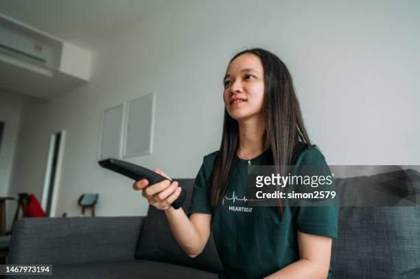 portrait of an asian woman changing tv channels at home - woman solitude stock pictures, royalty-free photos & images
