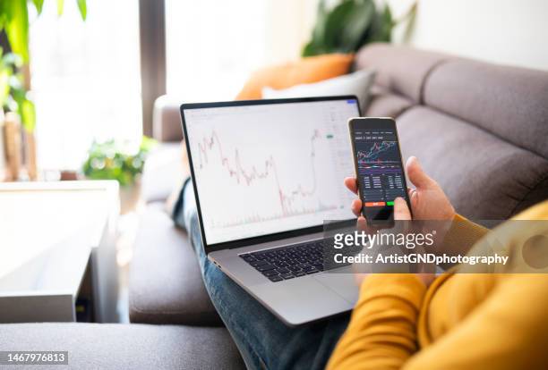 man buying cryptocurrency at home via laptop and phone. - bear and bull stock pictures, royalty-free photos & images