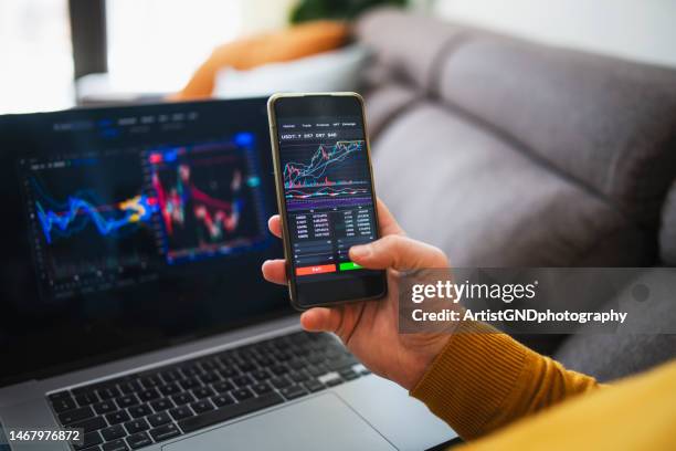 man buying cryptocurrency at home via laptop and phone. - cryptocurrency trading stock pictures, royalty-free photos & images