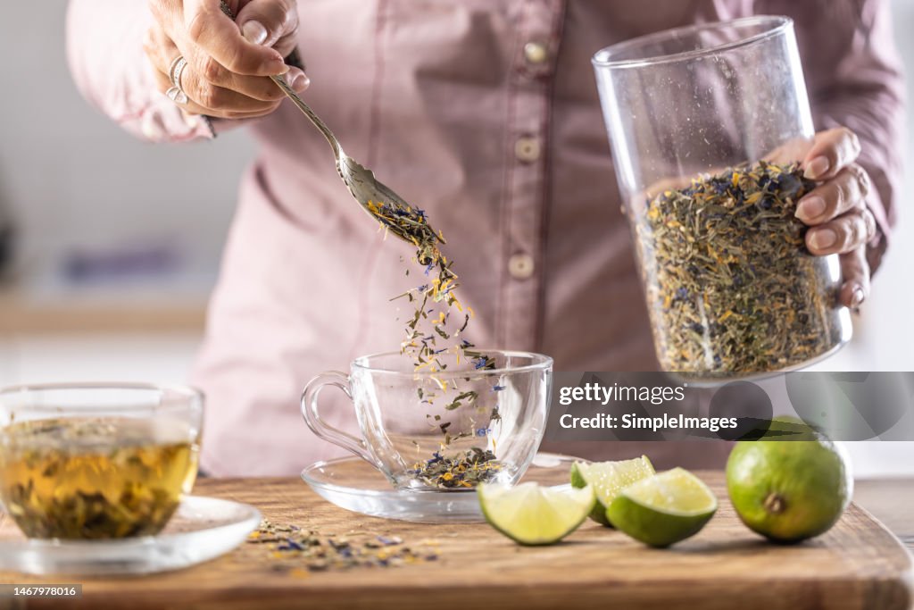 A woman pours dried tea leaves into a glass cup.