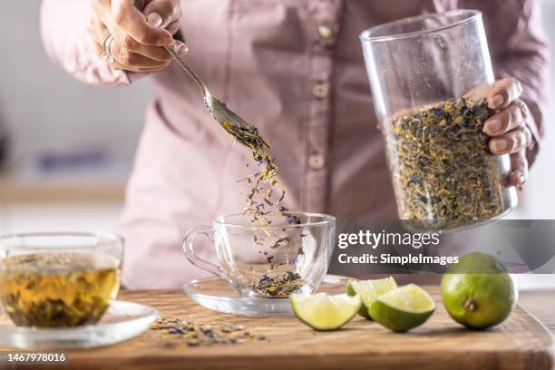 a woman pours dried tea leaves into a glass cup. - tisana foto e immagini stock