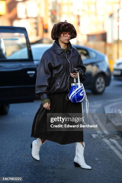 Guest wears brown fur hat, brown glasses, a black and green print pattern wool pullover, a black shiny leather oversized bomber coat, a black midi...