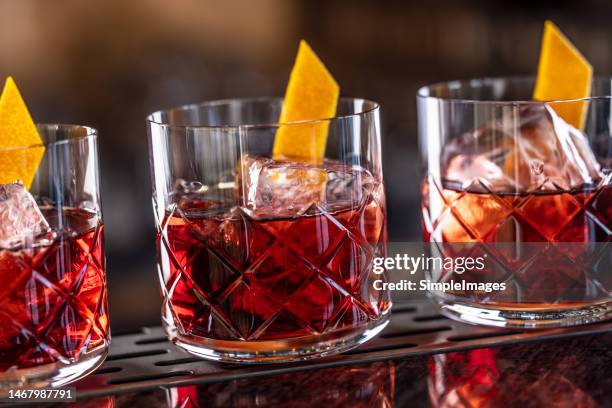 three modern glasses of negroni cocktail and gin short drink with sweet vermouth, red bitter liqueur and dried orange peel on bar counter. - liqueur - fotografias e filmes do acervo