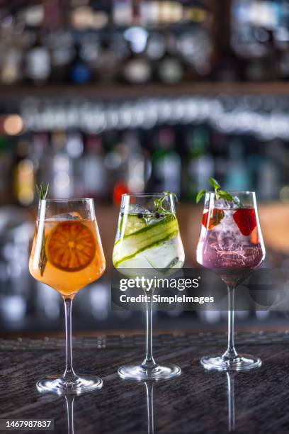 three colorful gin tonic cocktails in wine glasses on bar counter in pup or restaurant. - orange juice glass white background stock-fotos und bilder