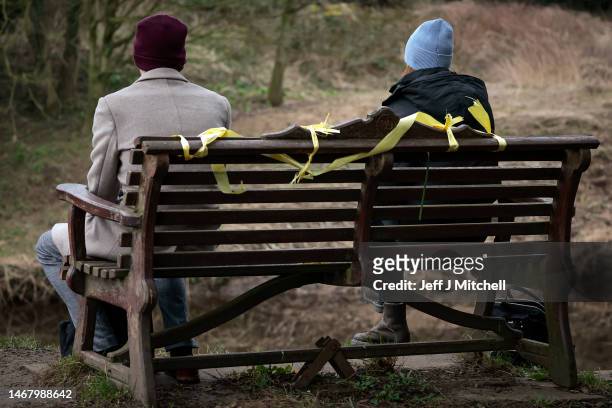 People sit on the bench which has some yellow ribbons adorning it, at the place where the phone of missing woman Nicola Bulley was found, next to the...