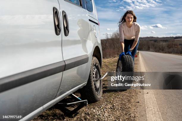 a young woman is changing a flat tire on her car on the road. - spare tyre stock pictures, royalty-free photos & images