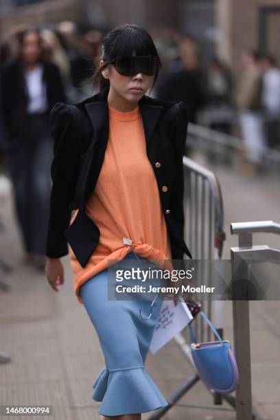 Susie Lau seen wearing a JW Anderson dress with an oversized black blazer, an orange shirt, a blue skirt, dark shades, a blue and purple patterned...