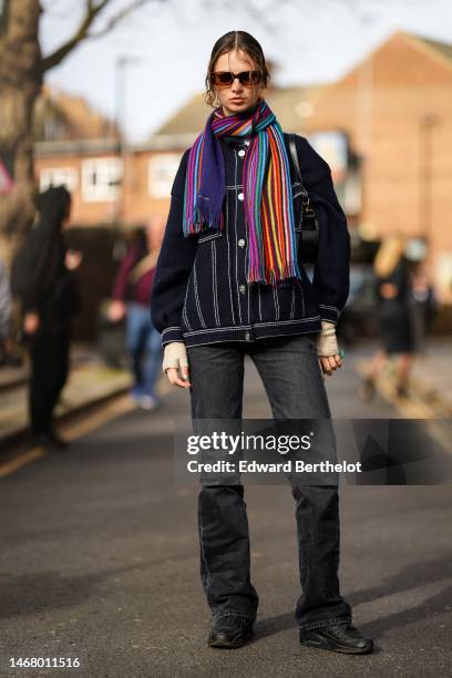 Model wears brown sunglasses, a multicolored print pattern wool long scarf, a navy blue denim buttoned jacket, dark gray denim large pants, black...