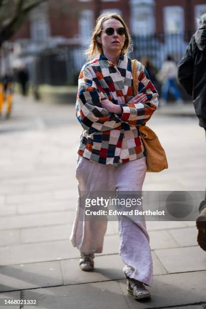 Guest wears black sunglasses, a camel / pale green / navy blue embroidered checkered pattern jacket, a beige cotton large shoulder bag, pale gray...