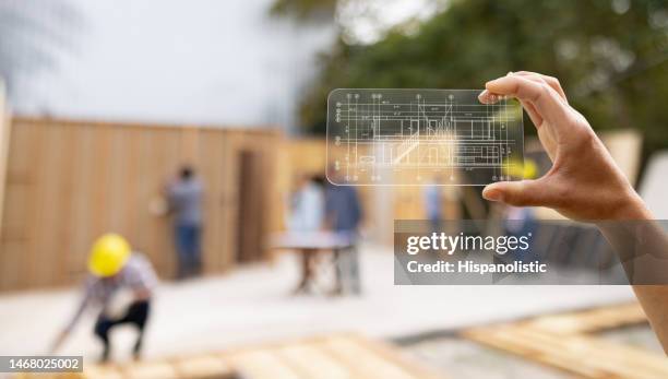 architekt auf einer baustelle betrachtet einen bauplan mit einem interaktiven bildschirm - smartphone hologram stock-fotos und bilder