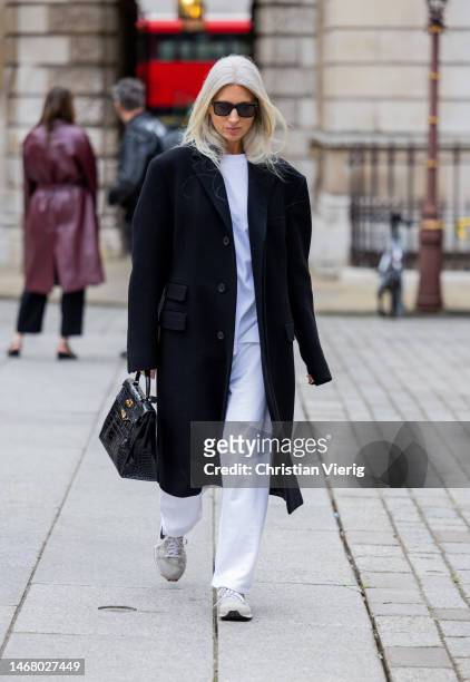 Sarah Harris wears black coat, Hermes bag, white pants, shirt, sneaker outside Emilia Wickstead during London Fashion Week February 2023 on February...