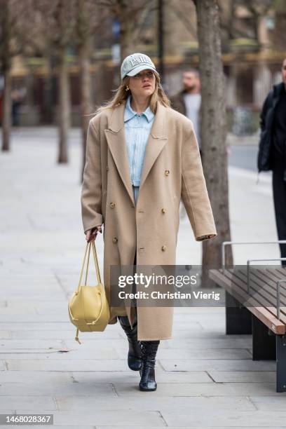 Guest wears beige oversized double breasted coat, cap, denim jacket with zipper light brown bag, black varnished boots, pants, skirt outside Yuzefi...