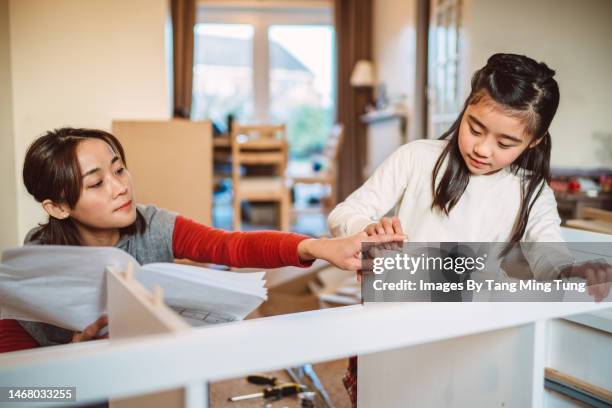 lovely cheerful girl helping her mom to assemble furniture in their new home - ikea stock pictures, royalty-free photos & images