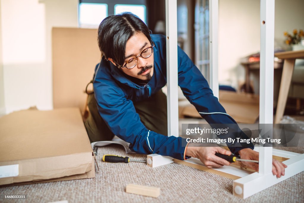 Young handsome man assembling furniture in his new home