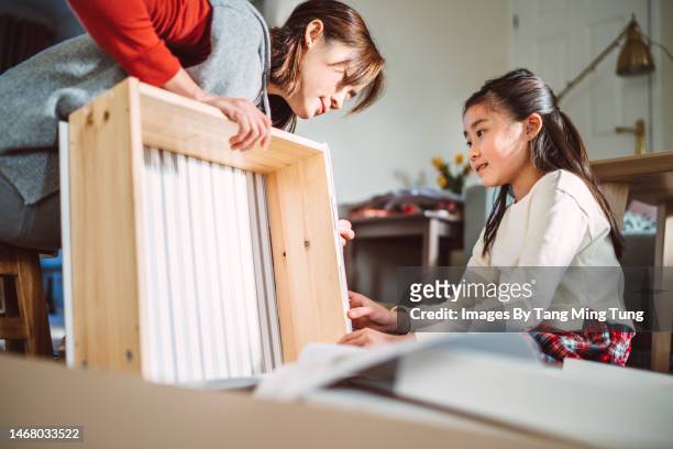 Lovely cheerful girl helping her mom to assemble furniture in their new home