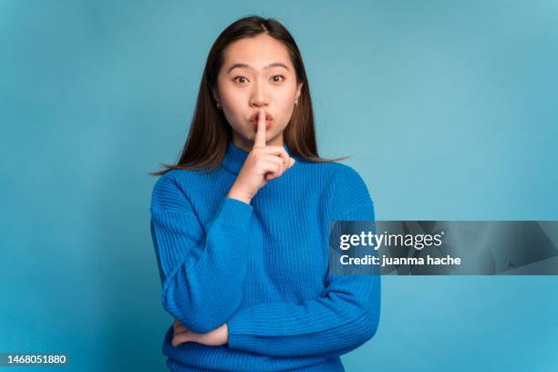 young woman with finger on lips and looking at camera in studio. silence gesture - finger on lips stock pictures, royalty-free photos & images