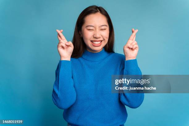 cheerful asian woman pointing at camera crossing fingers - sorte imagens e fotografias de stock