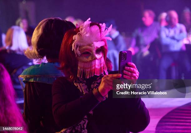Masked reveler takes a video of members of Brazilian Banda Toque de Classe dancing during the Band performance of carnival rhythms in Lounge D of...