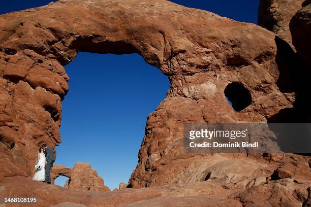Wedding couple kisses in front of sandstone formations with a blue sky at Arches National Park on September 24, 2022 in Moab, Utah.