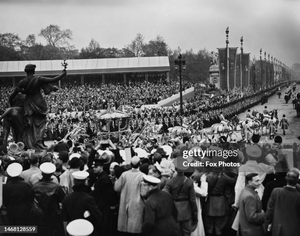 The Gold State Coach, in which British Royals George VI and Queen Elizabeth are riding, approaches The Mall, lined with Coldstream Guards and crowds...