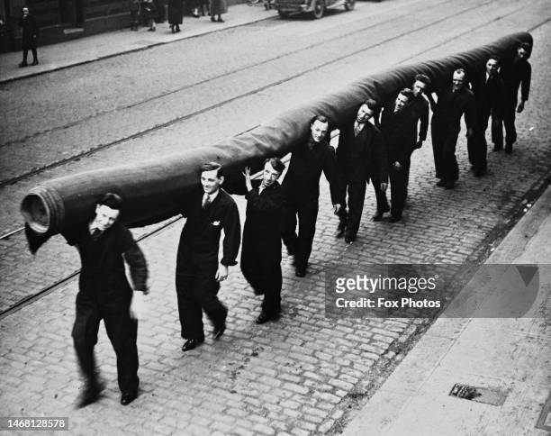 Ten workers carry a section of Coronation carpet to the packing room at the factory of James Templeton & Co on Glasgow Green in Glasgow, Scotland,...