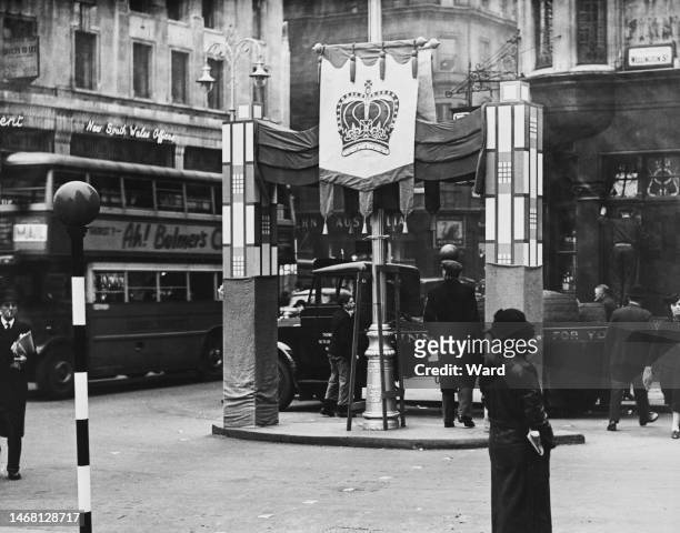 The first of the double standard-bearers on street refuges erected, as preparations are made ahead of the coronation of George VI and Queen...