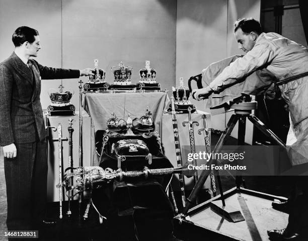 Man points at a row of three crowns among a display of the Crown Jewels as a second man, an camera operator, films the display of royal ceremonial...