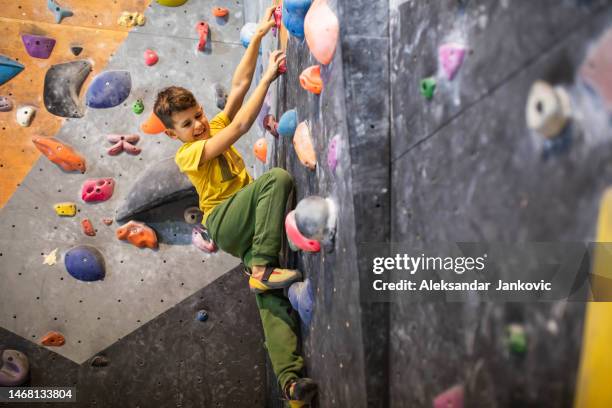 a cute boy climber straining to solve a boulder problem - bouldern indoor stock pictures, royalty-free photos & images