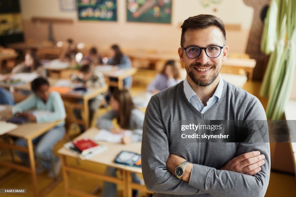 Happy elementary teacher in front of his students in the classroom.