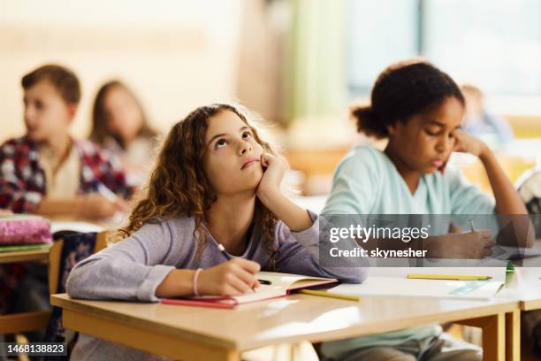 bored schoolgirl writing on a class at elementary school. - boredom stock pictures, royalty-free photos & images