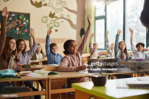 studenti elementari felici che alzano le mani su una classe a scuola. - child learning foto e immagini stock